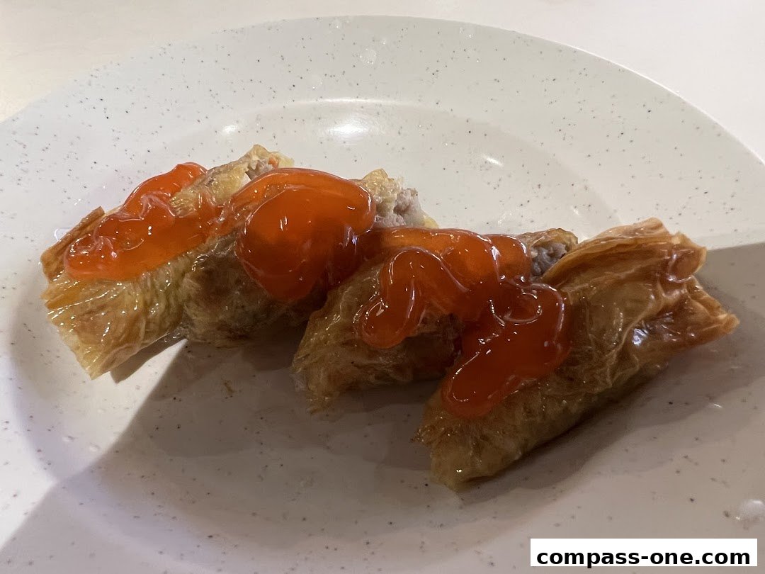 Three pieces of crispy fried tofu skin rolls topped with a vibrant orange sauce on a speckled white plate.