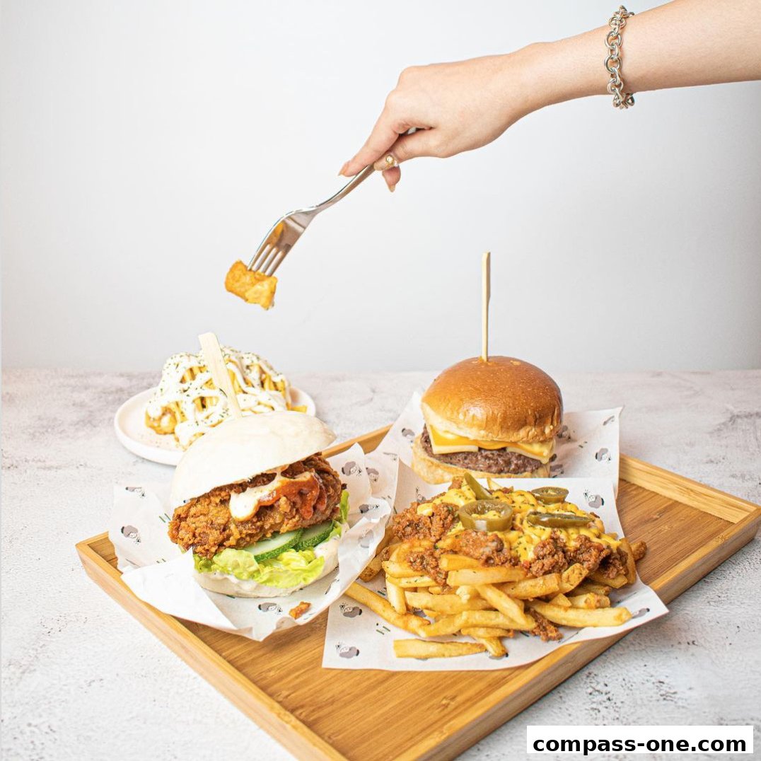 A hand uses a fork to pick up a tater tot from a spread of burgers and loaded fries.