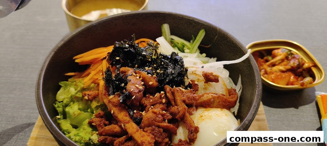 A close-up of a Korean bibimbap dish with chicken, vegetables, and a side of kimchi.