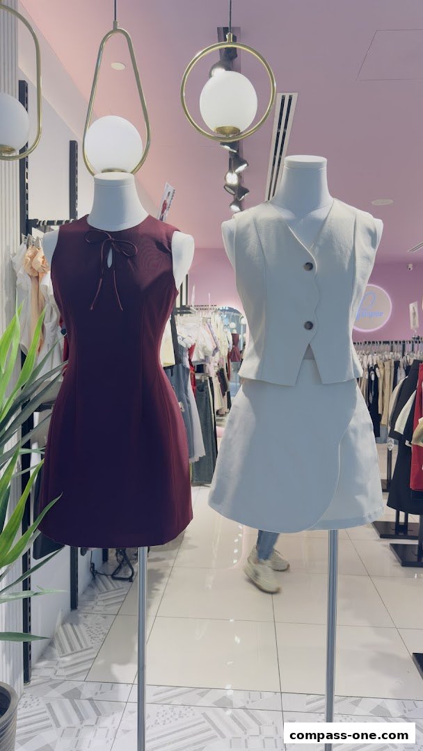 Two mannequins display stylish outfits inside a boutique with clothing racks in the background.
