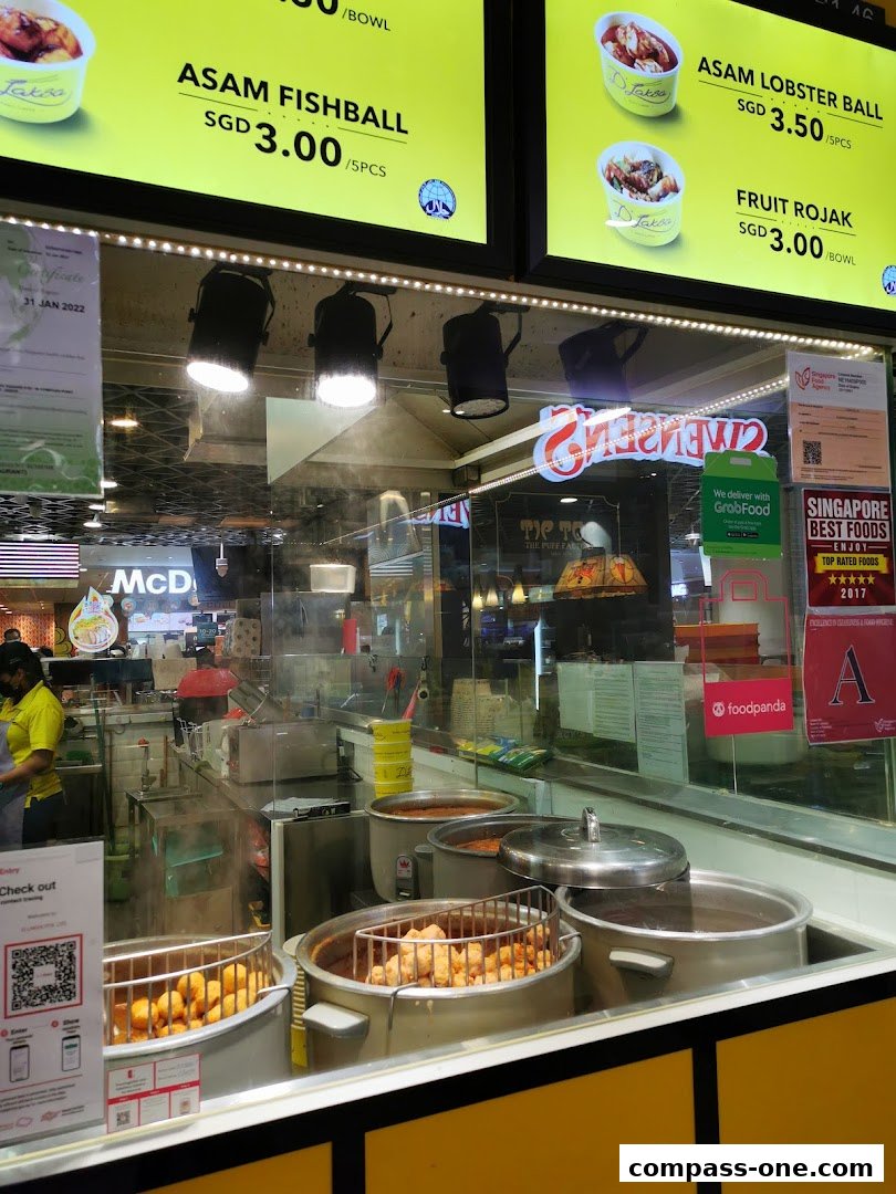 A food stall display featuring menu items like Asam Fishball and Fruit Rojak with prices.
