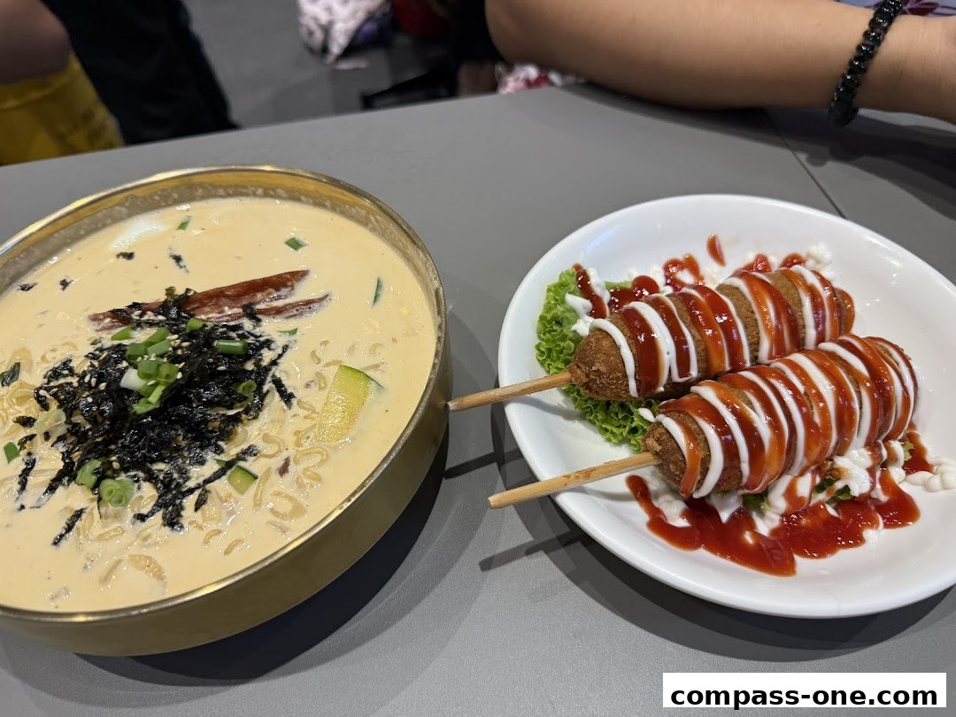 A bowl of creamy Korean noodle soup and two corn dogs drizzled with sauces.