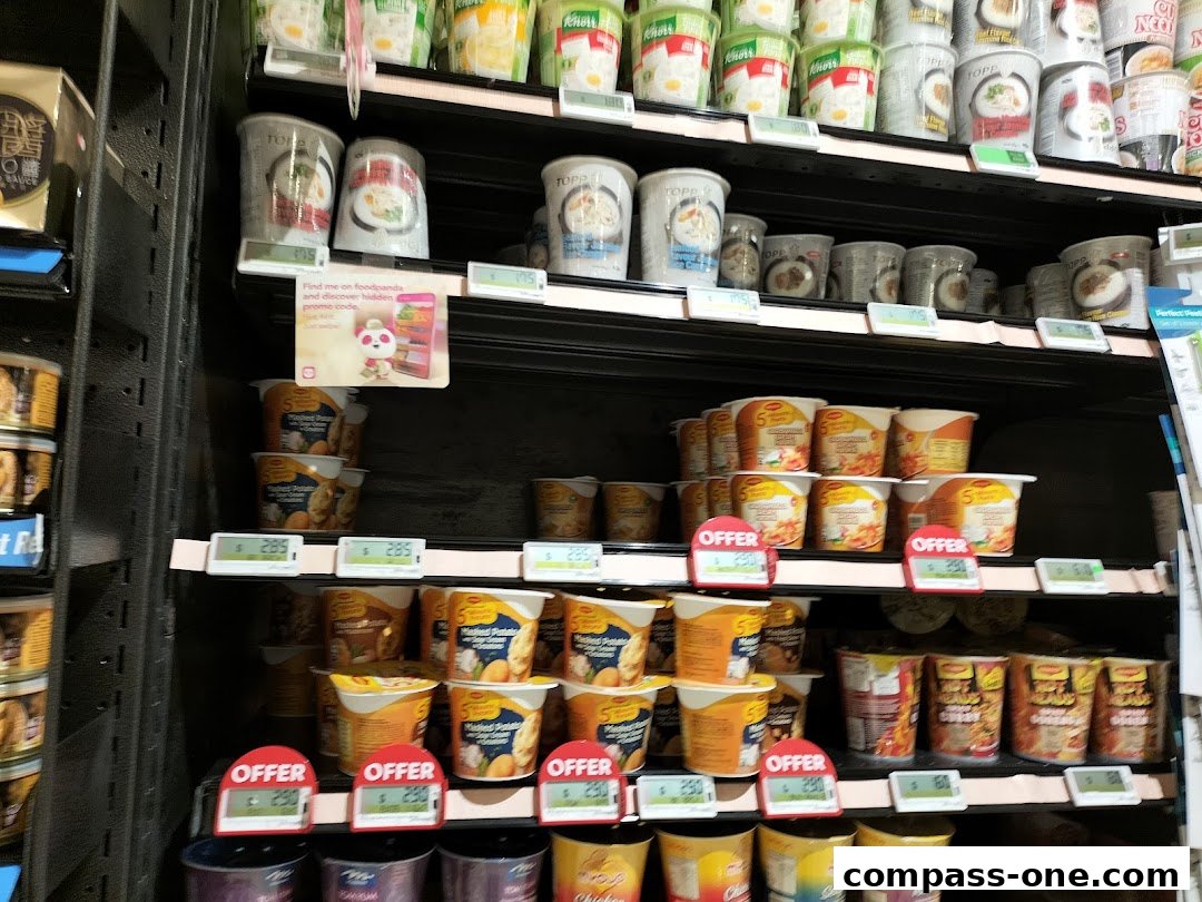 Shelves stocked with various instant noodle cups and other food items, some with offer tags.