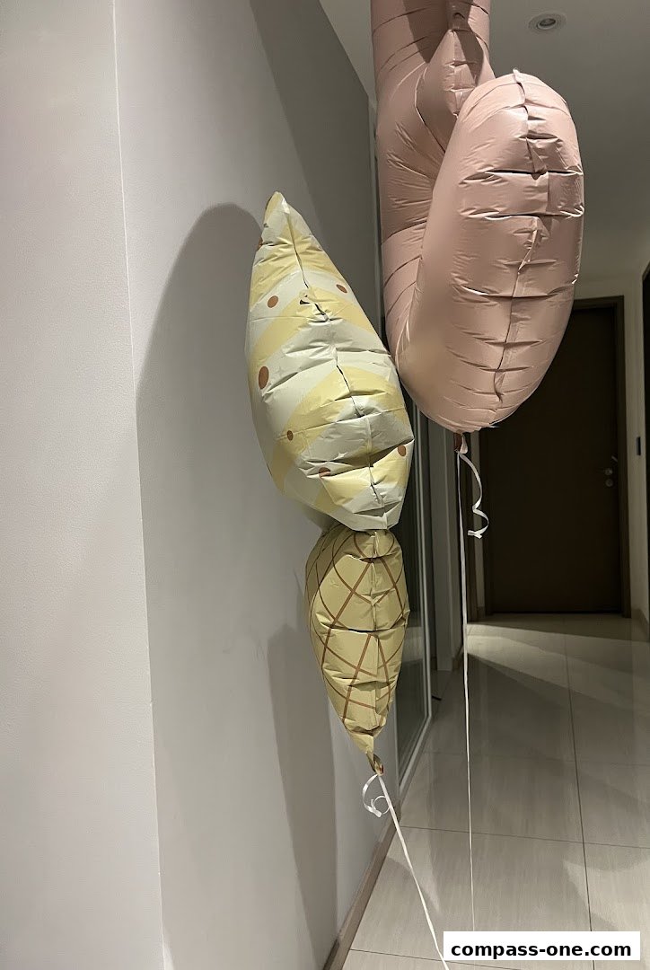 Three balloons, two patterned and one plain pink, are hanging indoors.
