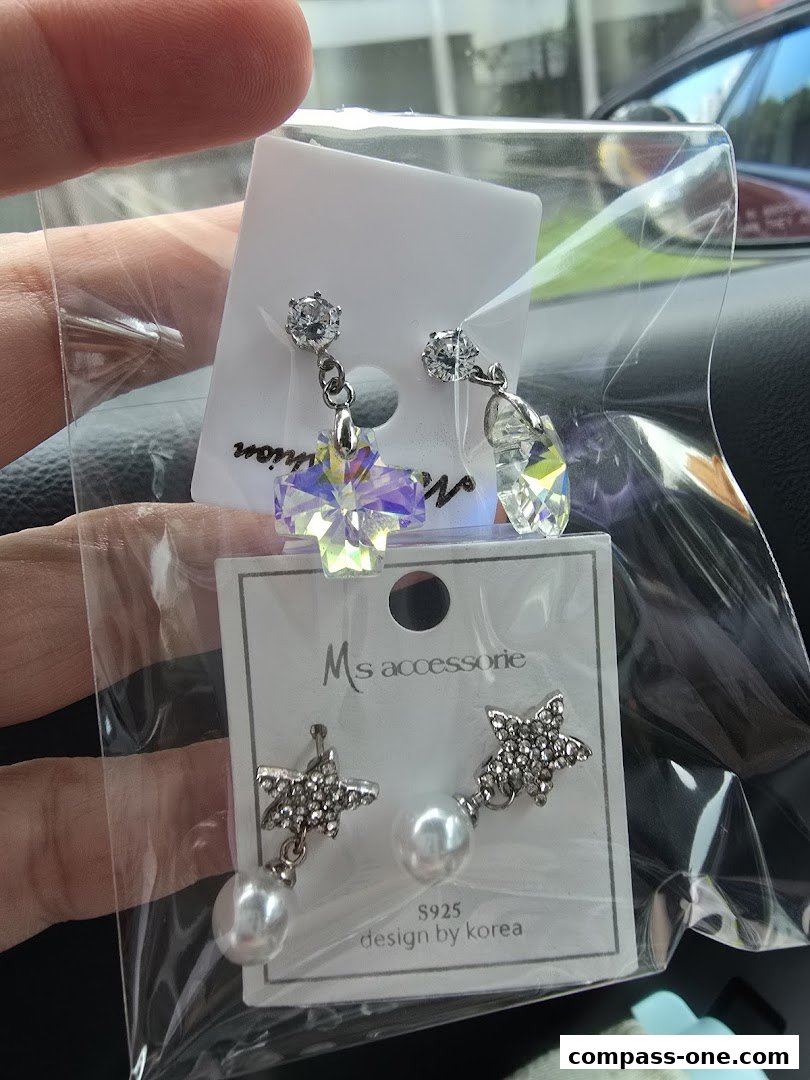 A hand holds two pairs of sparkling earrings, one with a cross shape and the other with stars and pearls.