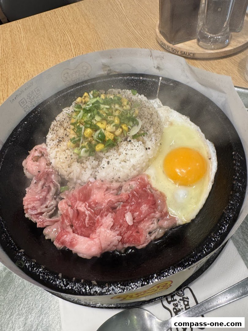 A sizzling hot plate meal with rice, beef, a fried egg, and corn, served at Pepper Lunch.