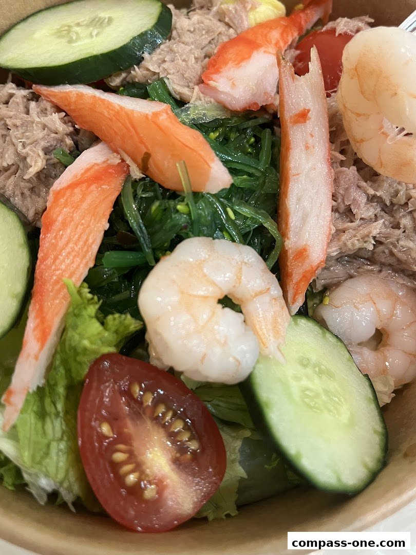 A close-up of a healthy salad with shrimp, imitation crab, tuna, seaweed, cucumber, and tomato.