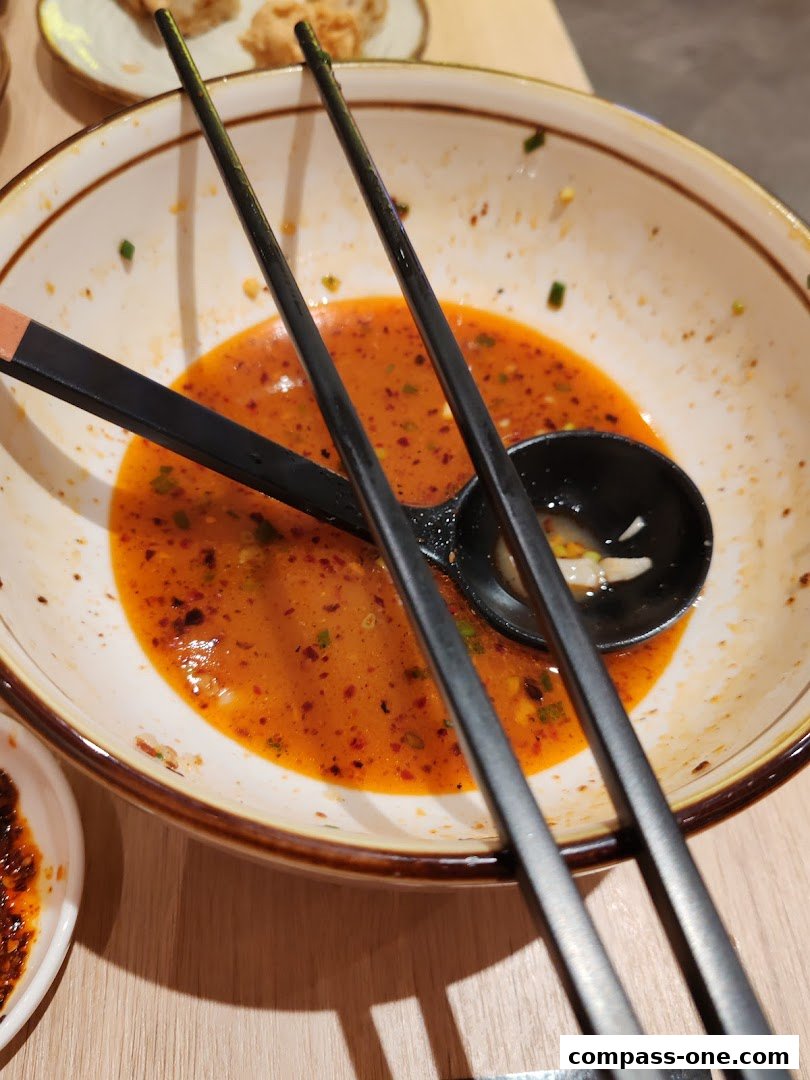 A close-up of a nearly empty ramen bowl with chopsticks and a spoon, showing leftover broth.