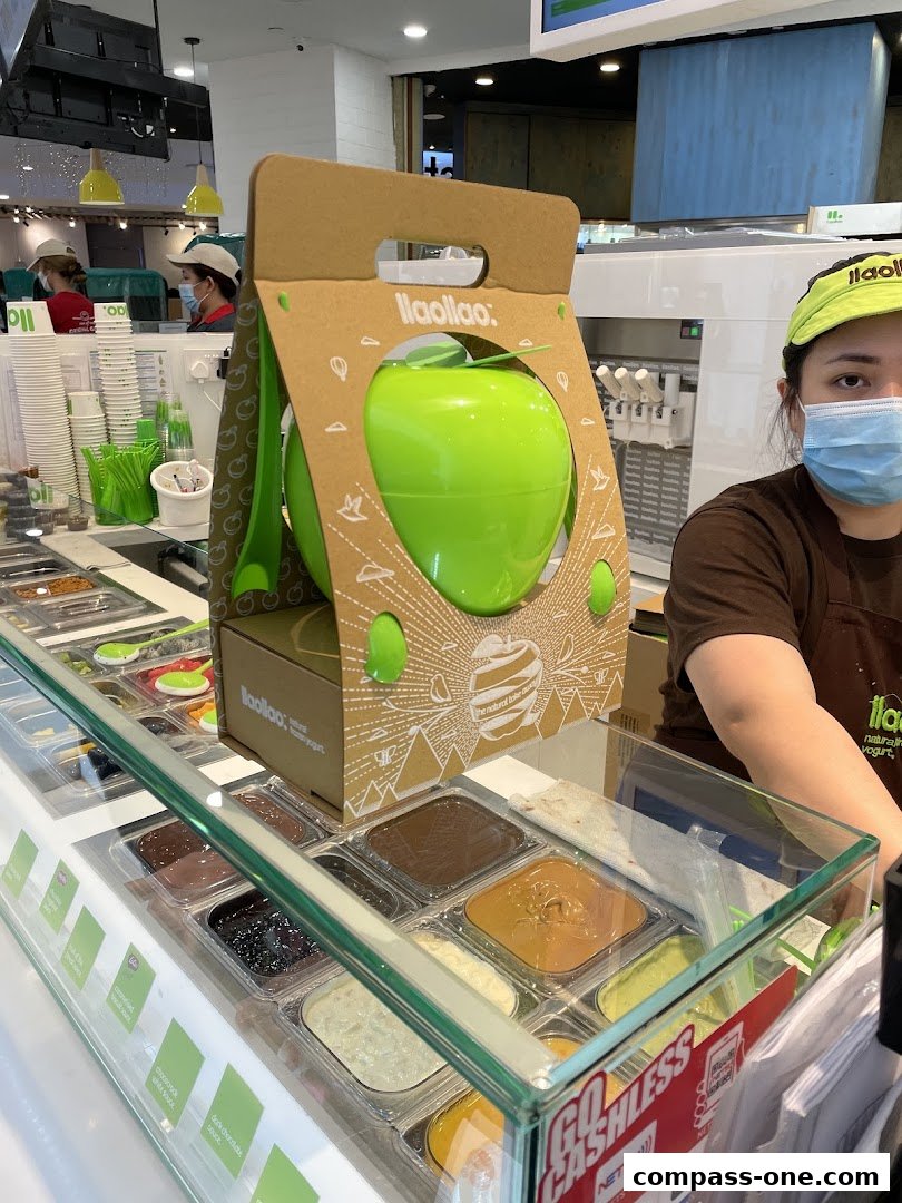 A llaollao shop counter with frozen yogurt toppings and a staff member.