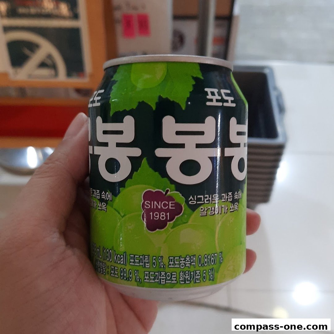 A hand holds a can of Bong Bong grape juice with visible grape imagery and text.