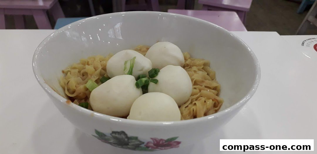 A close-up shot of a bowl of noodles with fish balls and chopped scallions.