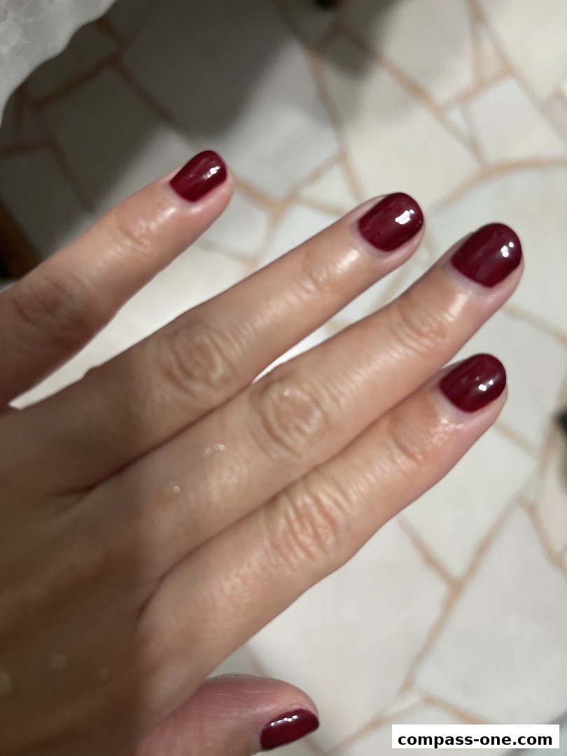 A close-up shot of a hand with perfectly manicured, glossy dark red nails.