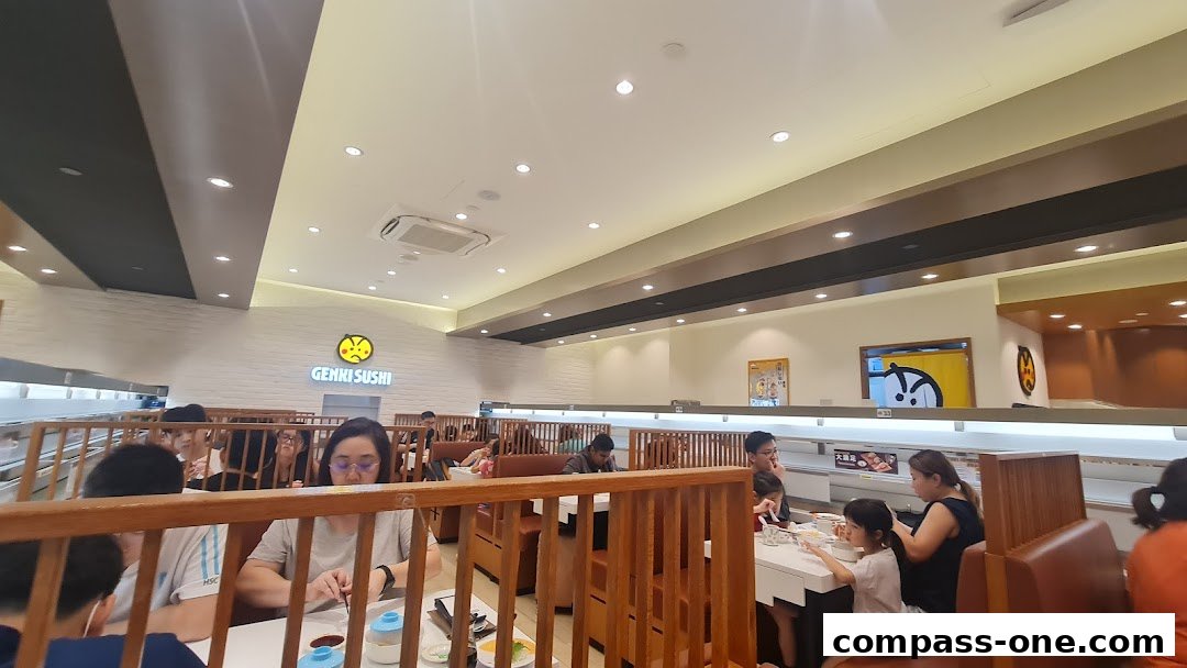 Interior view of Genki Sushi restaurant with customers dining at conveyor belt sushi tables.