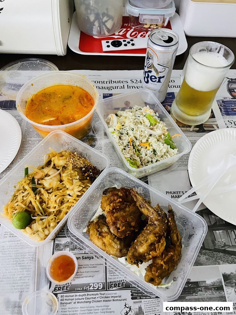 A spread of Thai food takeout containers, including fried chicken, Pad Thai, fried rice, soup, and a can of Tiger beer.