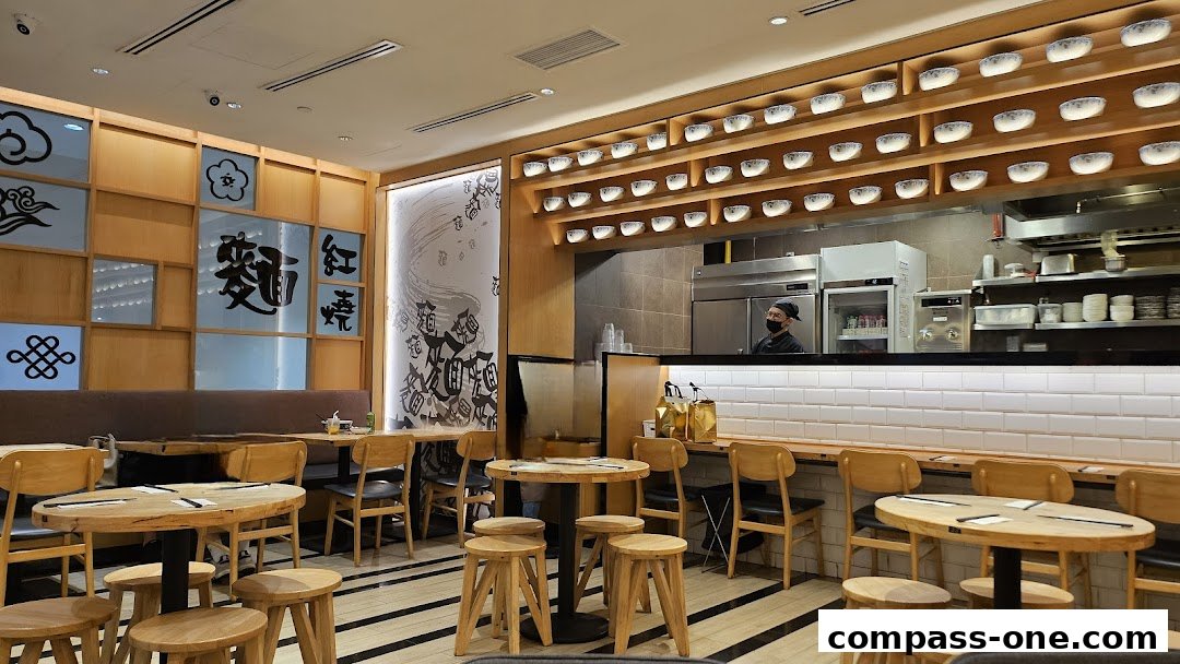 Interior of LeNu Chefs Wai Noodle Bar with wooden tables, chairs, and a view of the kitchen.