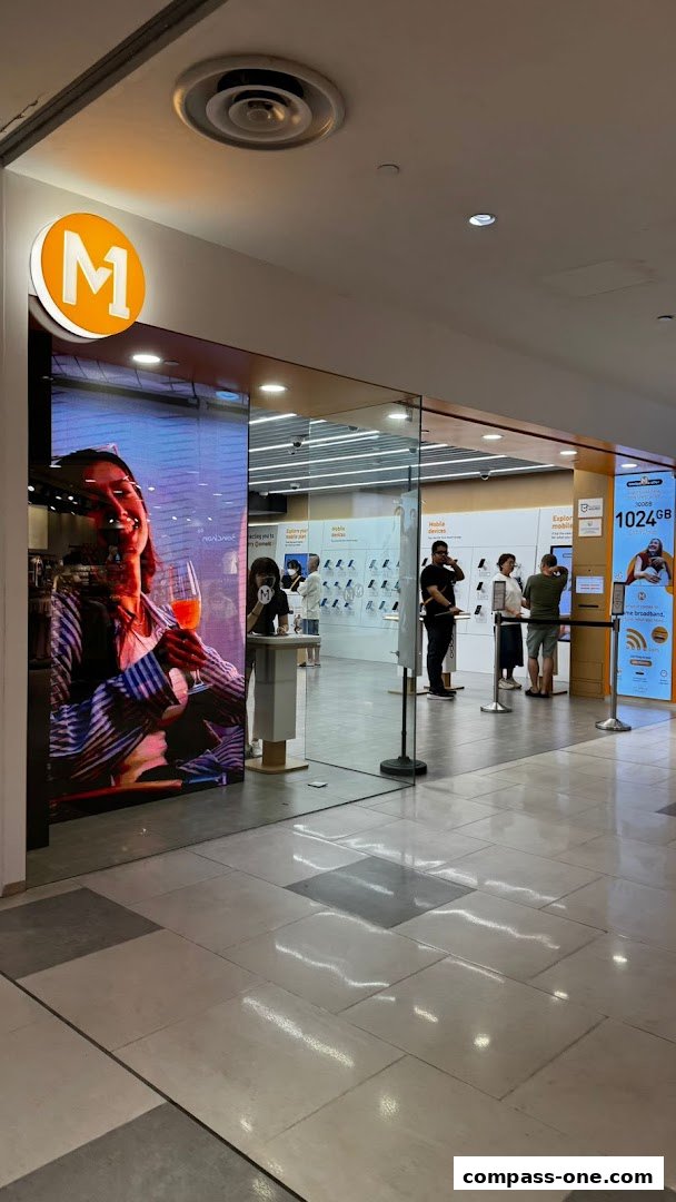 The entrance of an M1 phone shop and internet service provider with customers inside.