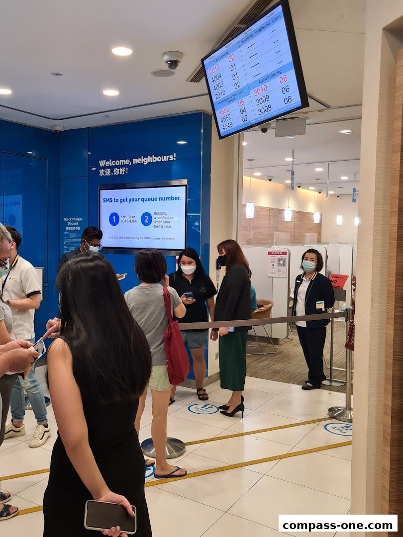 People queuing inside a POSB bank branch with a digital display showing queue numbers.