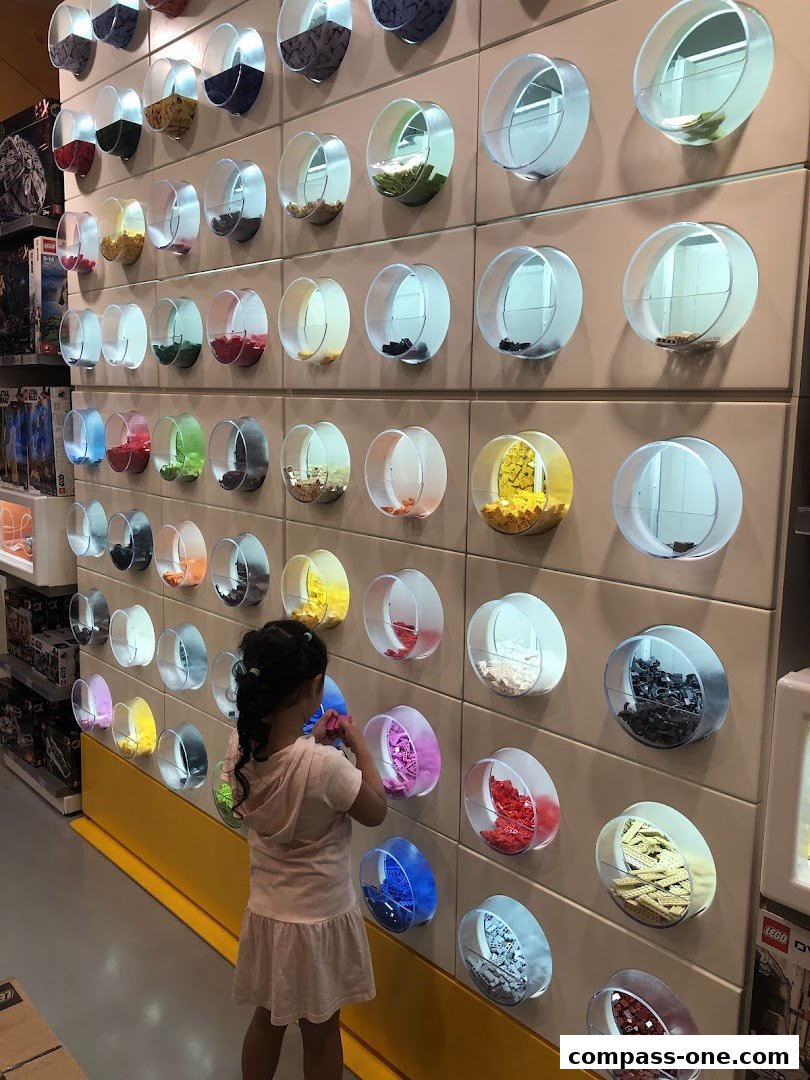 A young girl selects LEGO bricks from a colorful wall display at The Brick Shop.