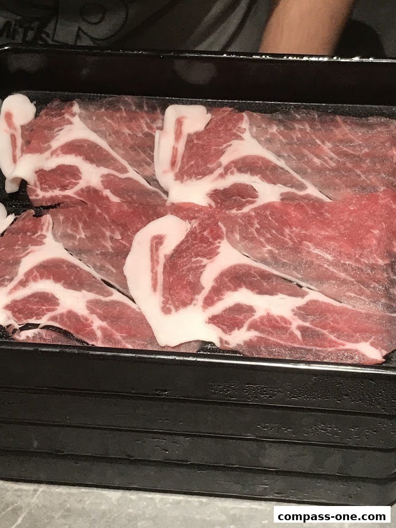 Thinly sliced marbled raw meat arranged in a black tray.