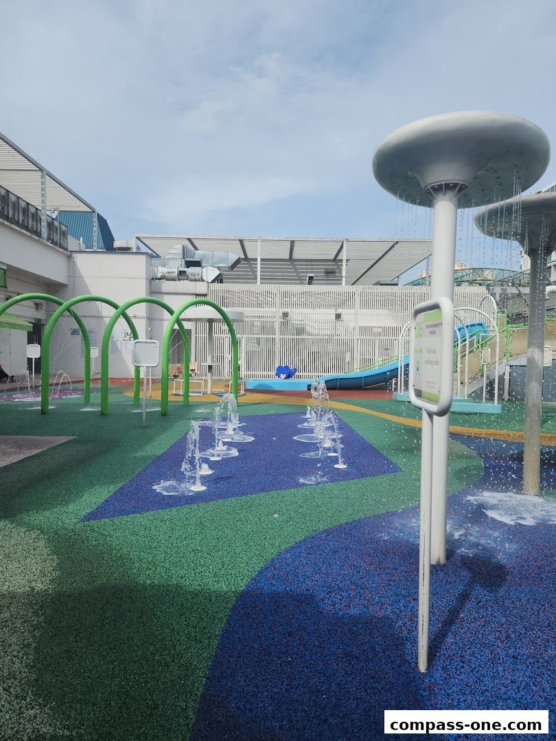 A colorful water playground with fountains and a slide under a partly cloudy sky.