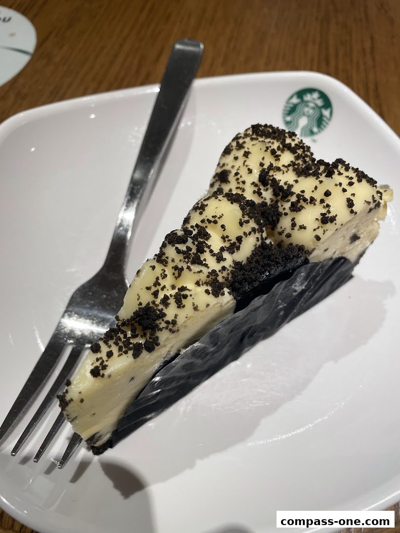 A slice of creamy cheesecake topped with crushed cookies on a white plate with a fork.