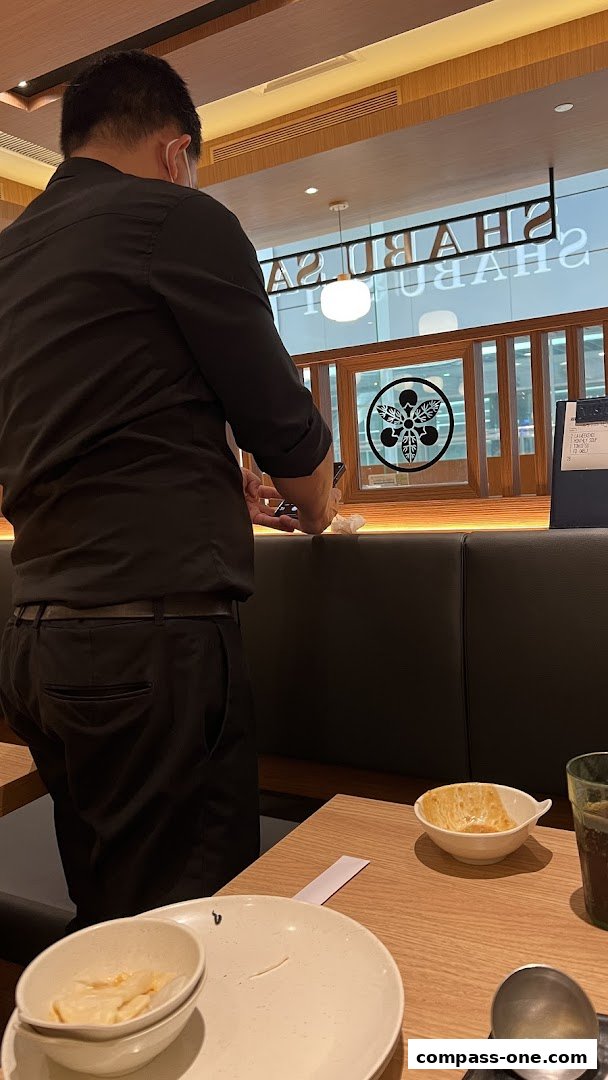 A server stands near a table with plates and bowls at Shabu Sai.