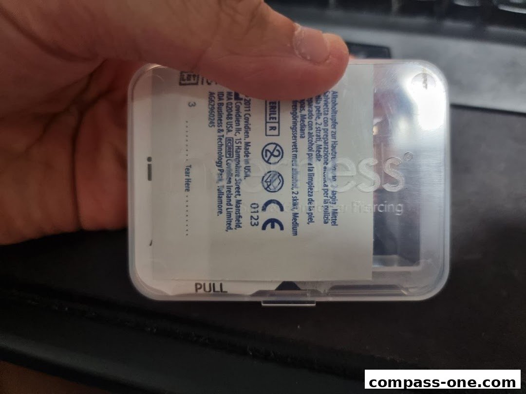 A hand holds a clear plastic case containing a sterile wipe for ear piercing.