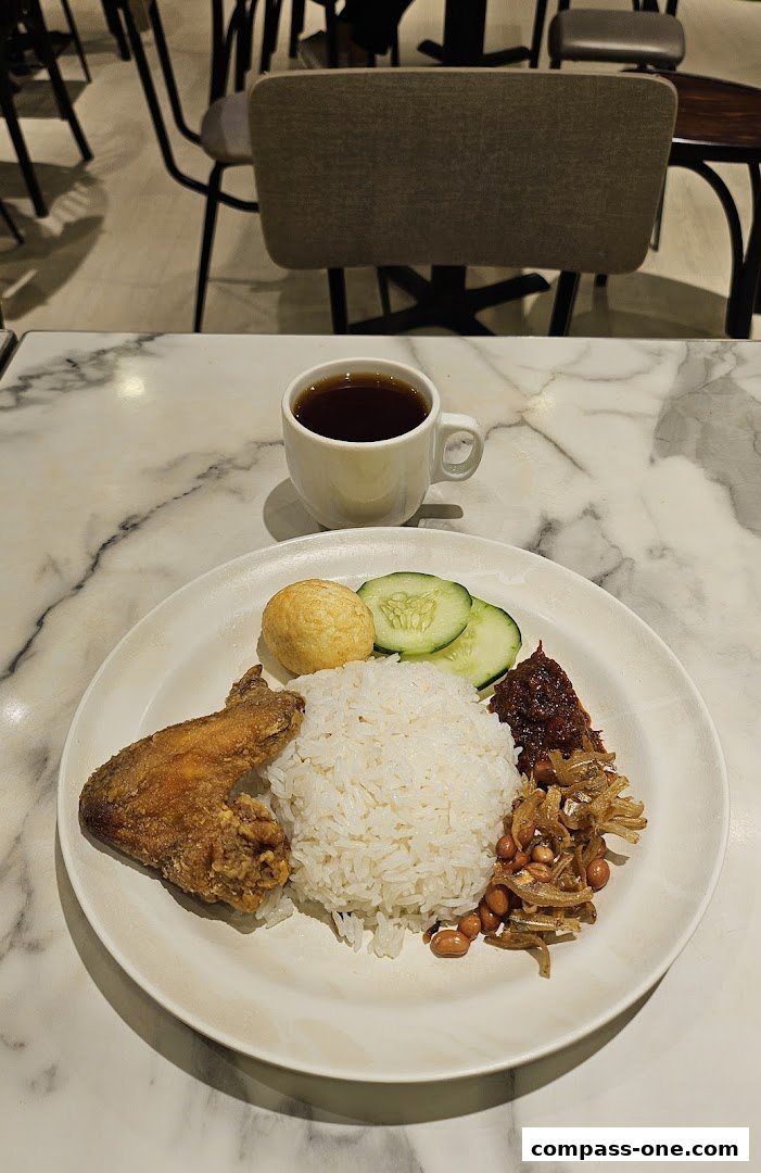 A plate of Nasi Lemak with fried chicken wing, rice, cucumber, and a cup of tea.