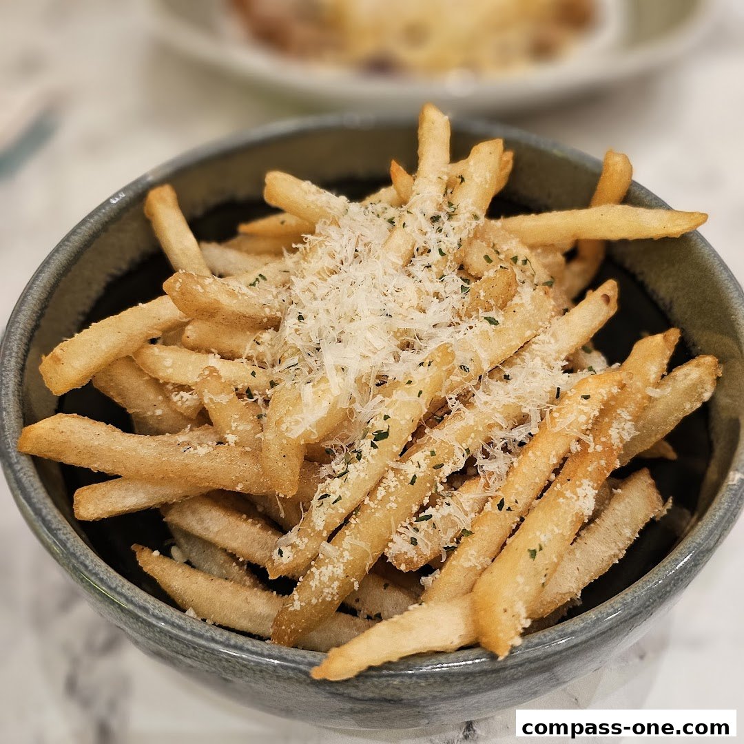 A close-up shot of a bowl of golden french fries topped with grated cheese and herbs.