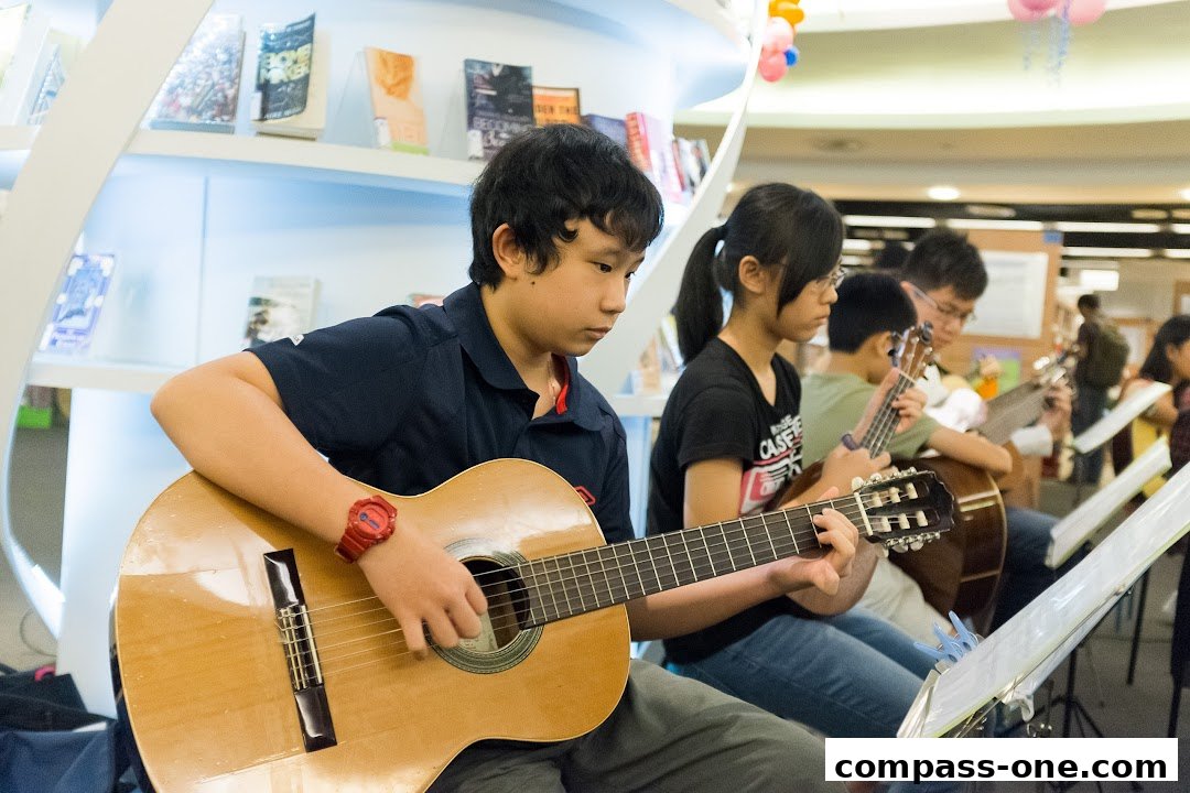 Students learning to play guitars and ukuleles in a music school setting.