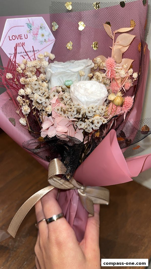 A hand holds a bouquet of preserved flowers with a 'Love U Mom' card.