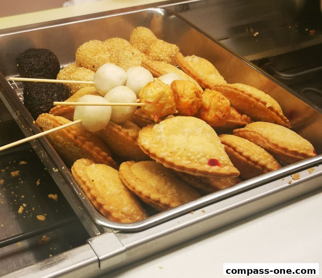 A close-up of a metal tray filled with various fried snacks on skewers and pastries.