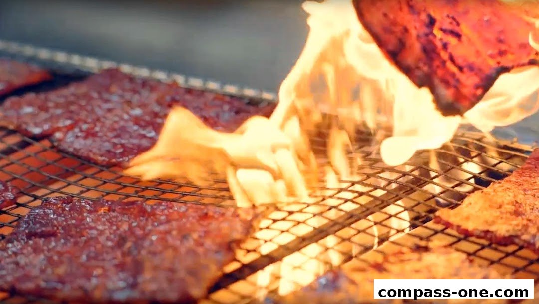 Close-up of bak kwa being grilled over an open flame on a wire rack.