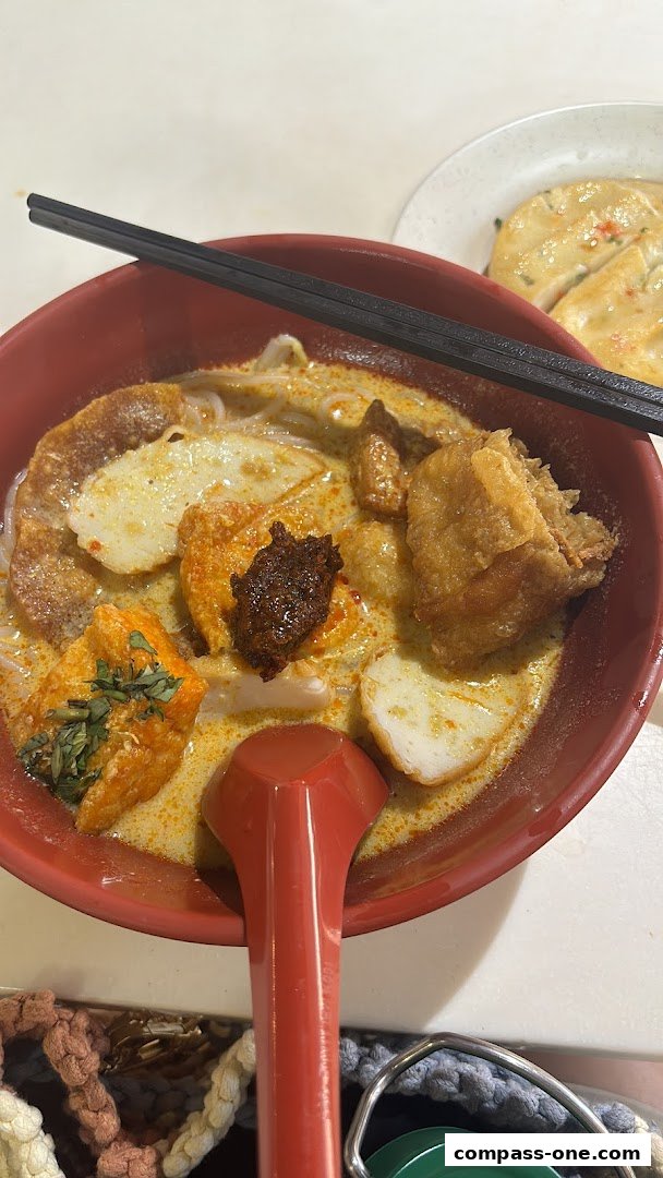 A close-up of a delicious bowl of Laksa with various toppings and a side dish.