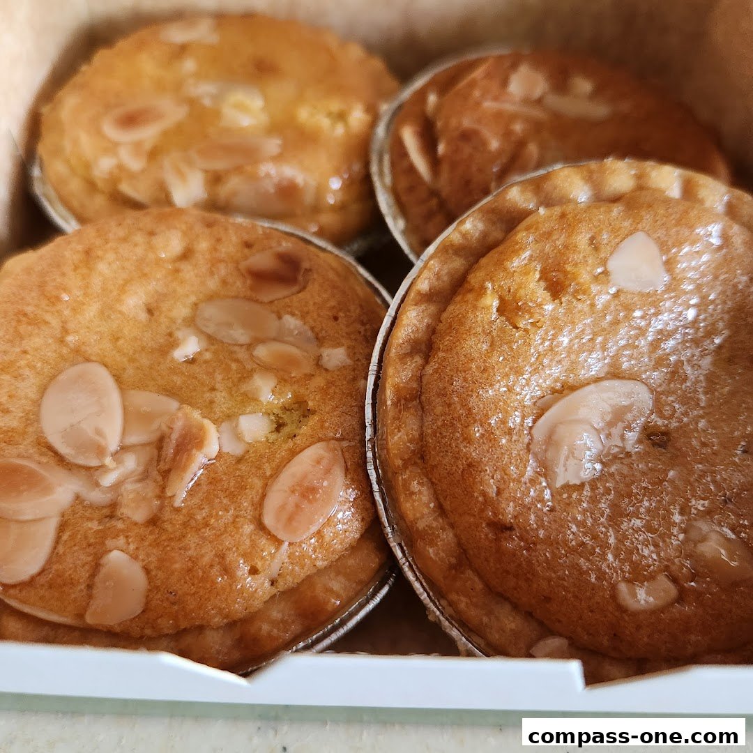 Close-up of four freshly baked almond tarts in foil cups.