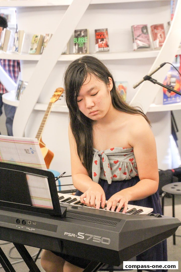 A young girl plays a keyboard in front of sheet music, with a guitar and books in the background.