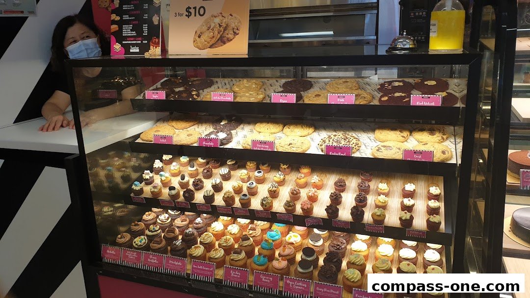 A display case filled with cookies and cupcakes, with a staff member behind the counter.