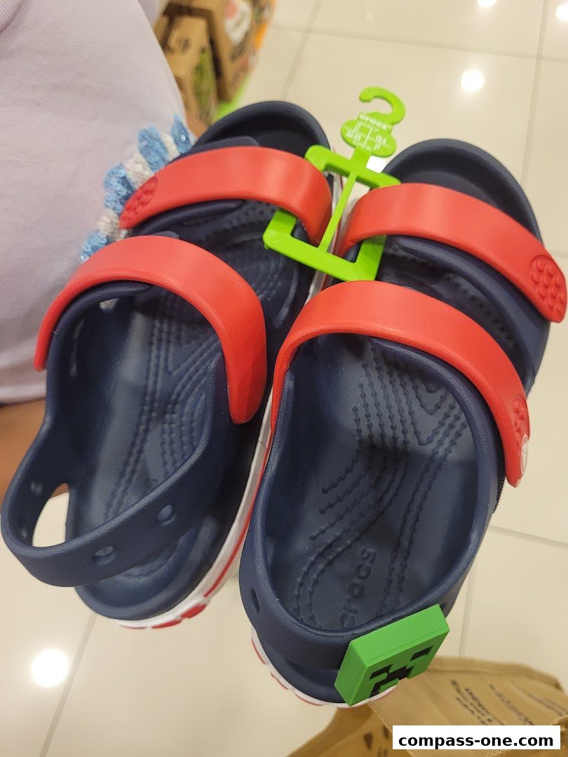 A pair of navy blue Crocs sandals with red straps and a Minecraft charm.