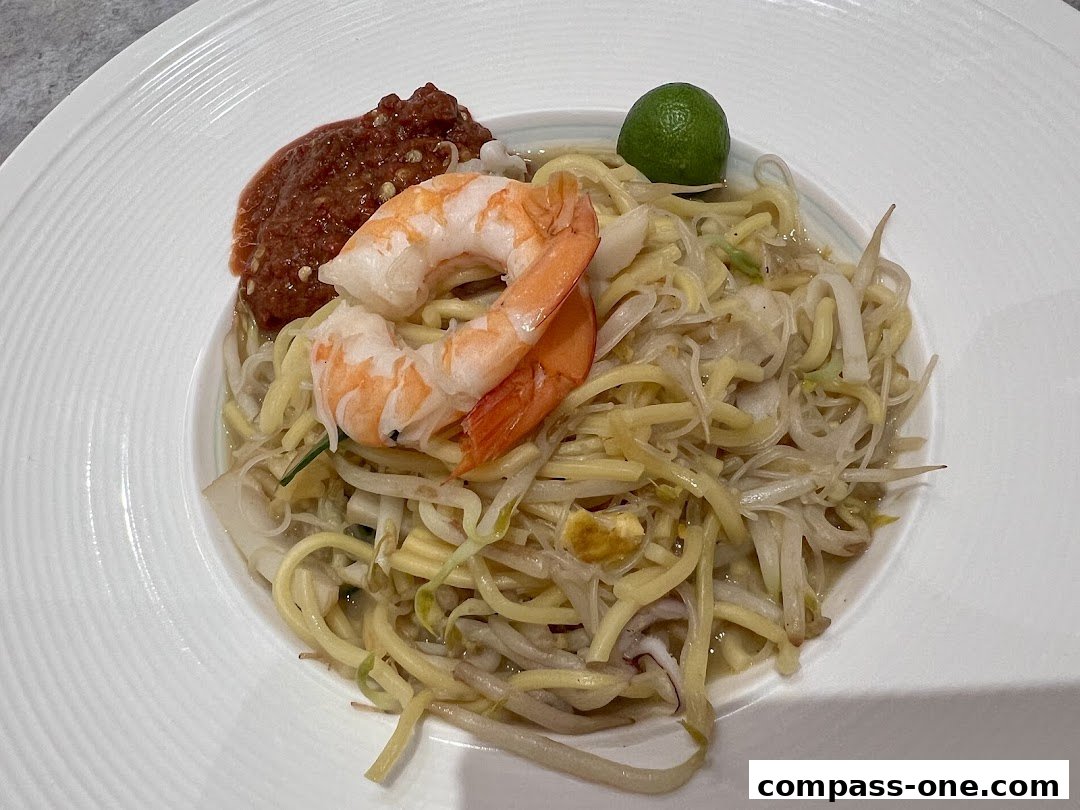 A close-up of a delicious noodle dish with shrimp, chili paste, and a lime wedge.