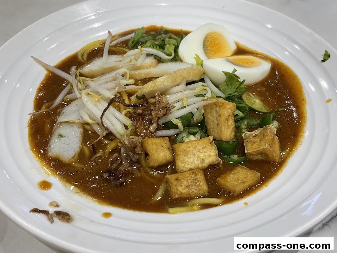 A close-up shot of a delicious bowl of Laksa with noodles, tofu, egg, and bean sprouts.