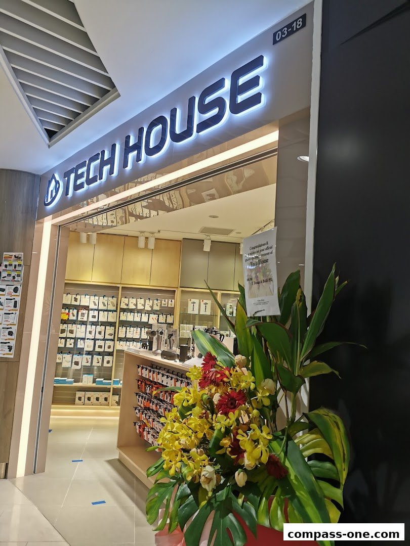 The entrance of a Tech House store with a large illuminated sign and a floral arrangement.