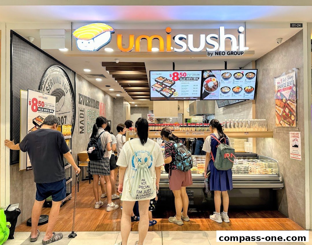 A group of people queuing at a Umi Sushi restaurant with a display of bento meals and donburi.