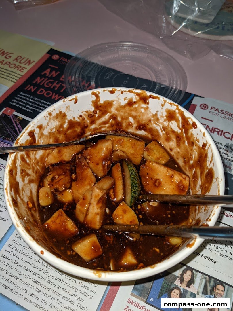 A bowl of food with a dark sauce, chopsticks, and a plastic lid on a table.