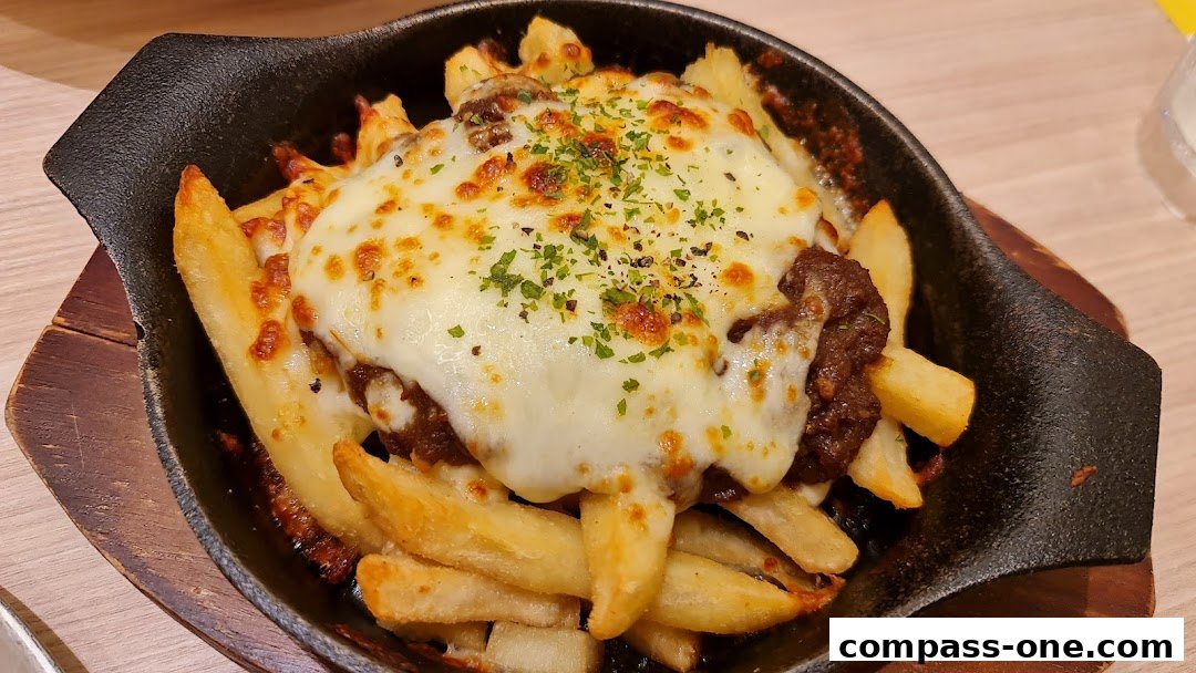 A close-up of cheesy fries topped with minced meat and herbs, served in a cast-iron dish.