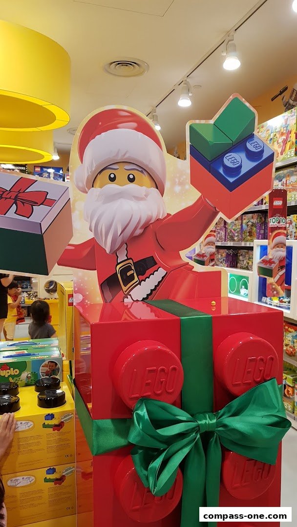 A festive LEGO display featuring Santa Claus and a giant gift box with a green bow.