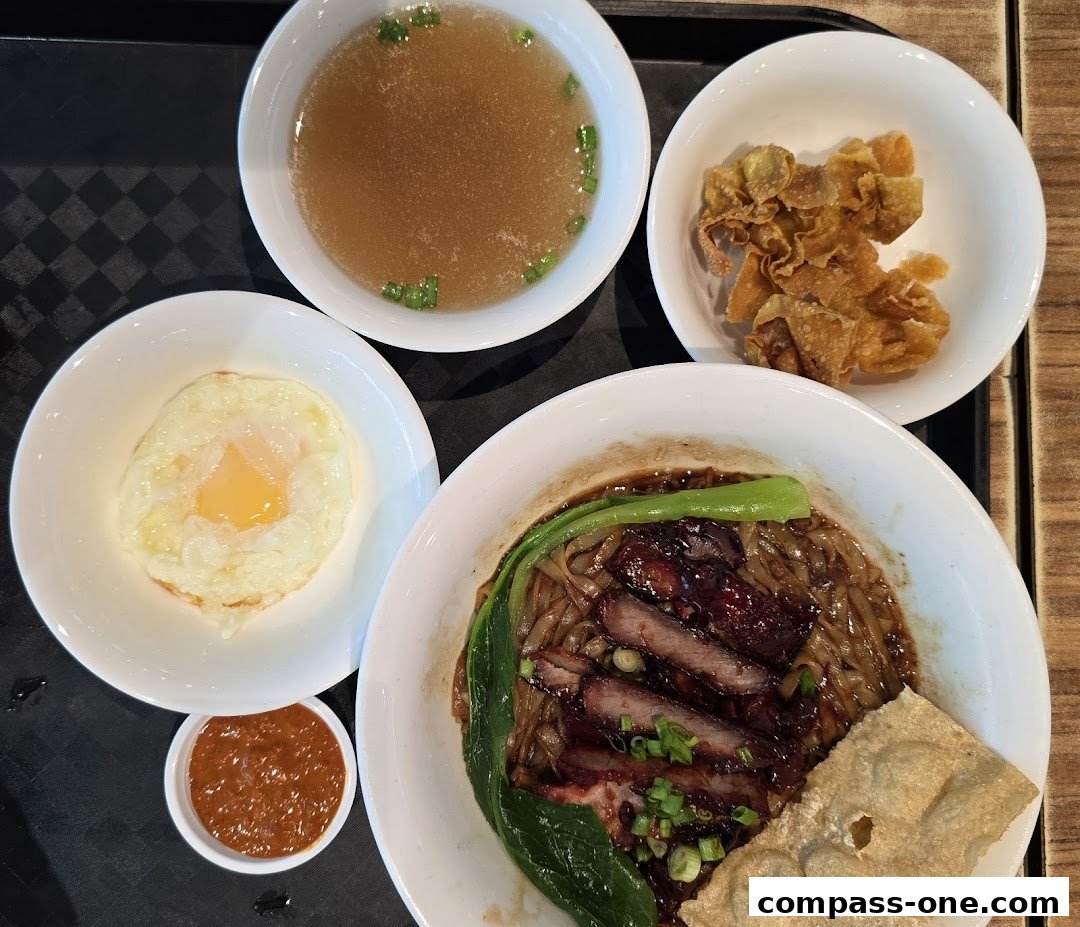 A bowl of Ipoh noodles with char siu, fried wontons, soup, and a fried egg.