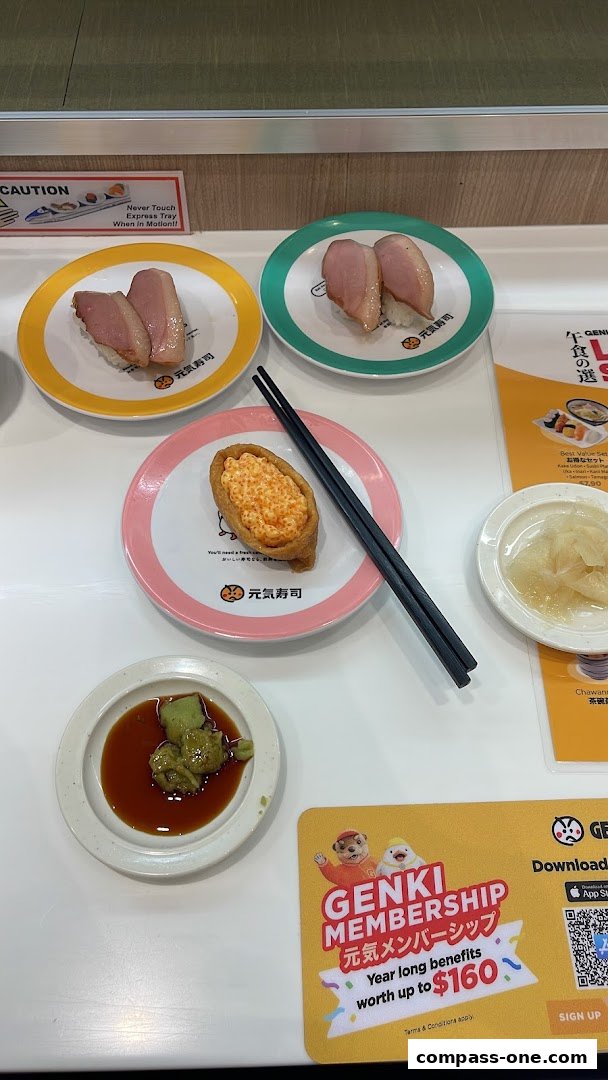Plates of sushi and a dipping sauce are arranged on a white table with a promotional sign.