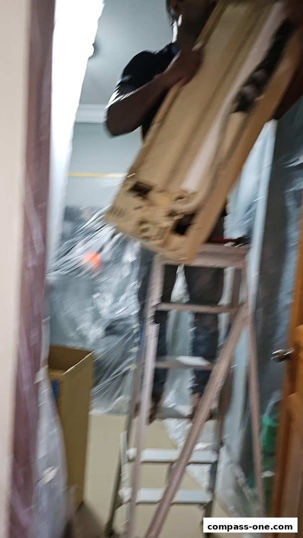 A person on a ladder is holding a large panel, possibly for installation or repair.