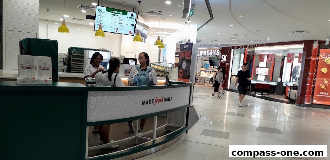 Krispy Kreme counter with staff serving customers and a beverage menu displayed overhead.