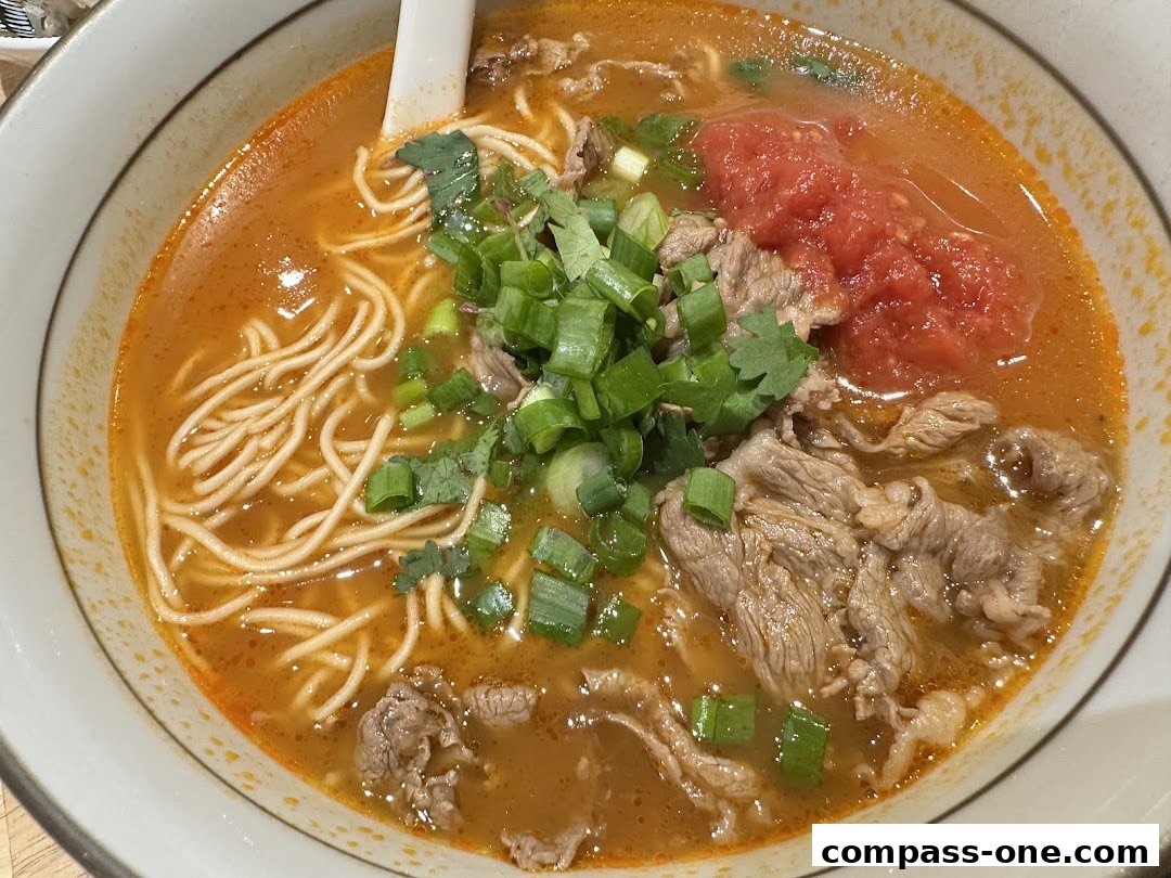 A close-up shot of a steaming bowl of beef noodle soup with tomatoes and scallions.